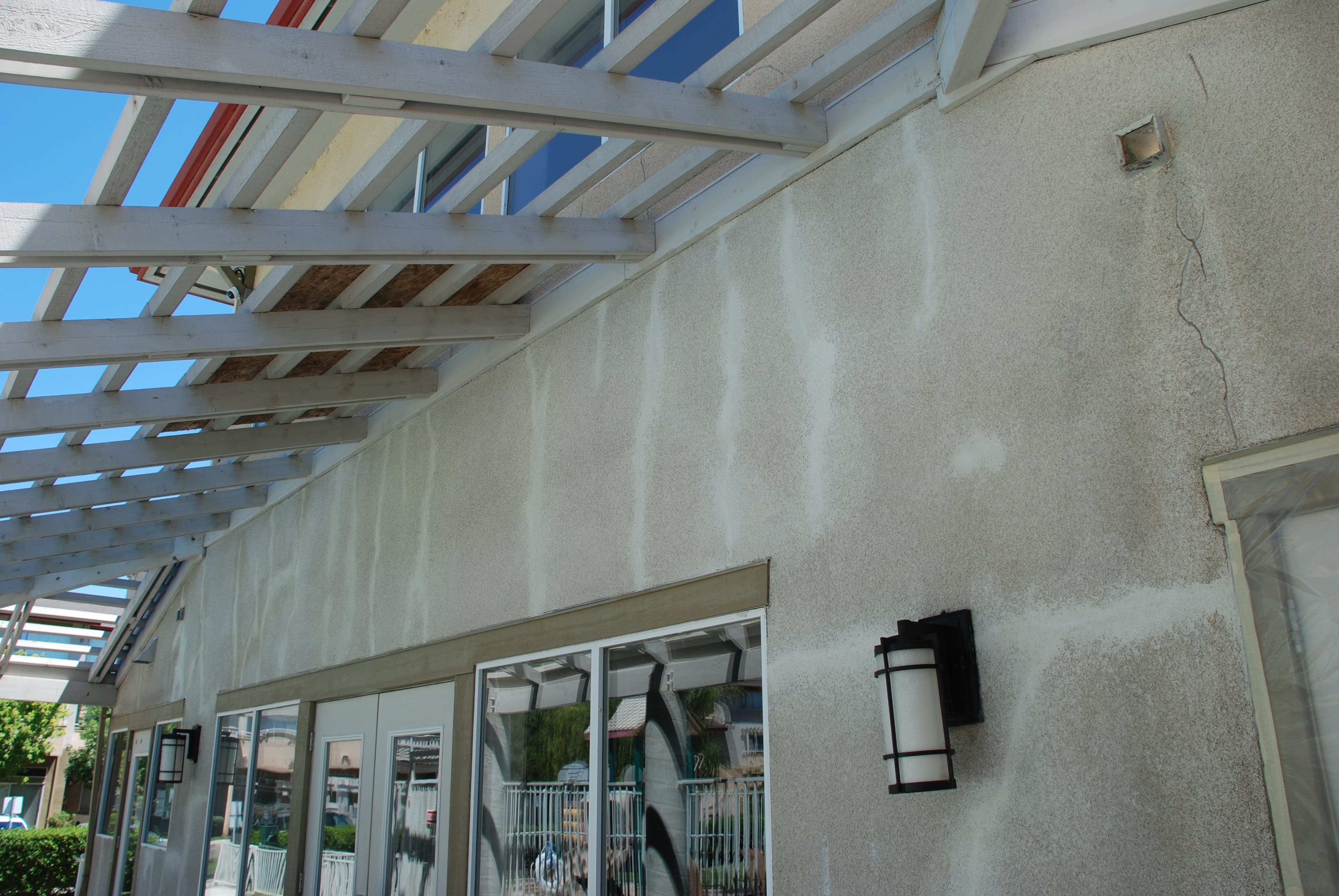 A stucco wall under a patio cover with repeating vertical crack lines patched during a repair