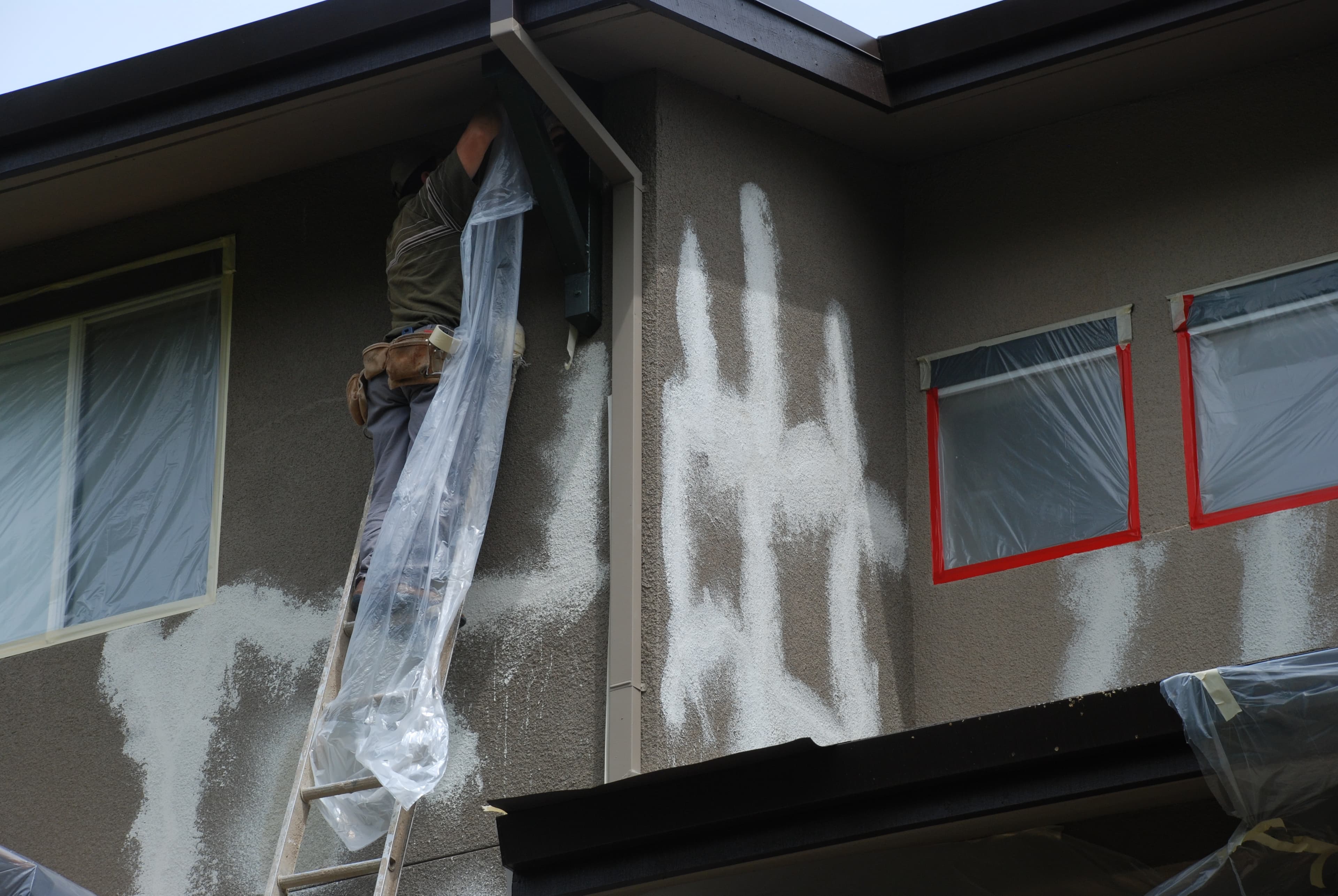 A HomePRO team member on a ladder working on stucco cracks around the windows of a two-story home