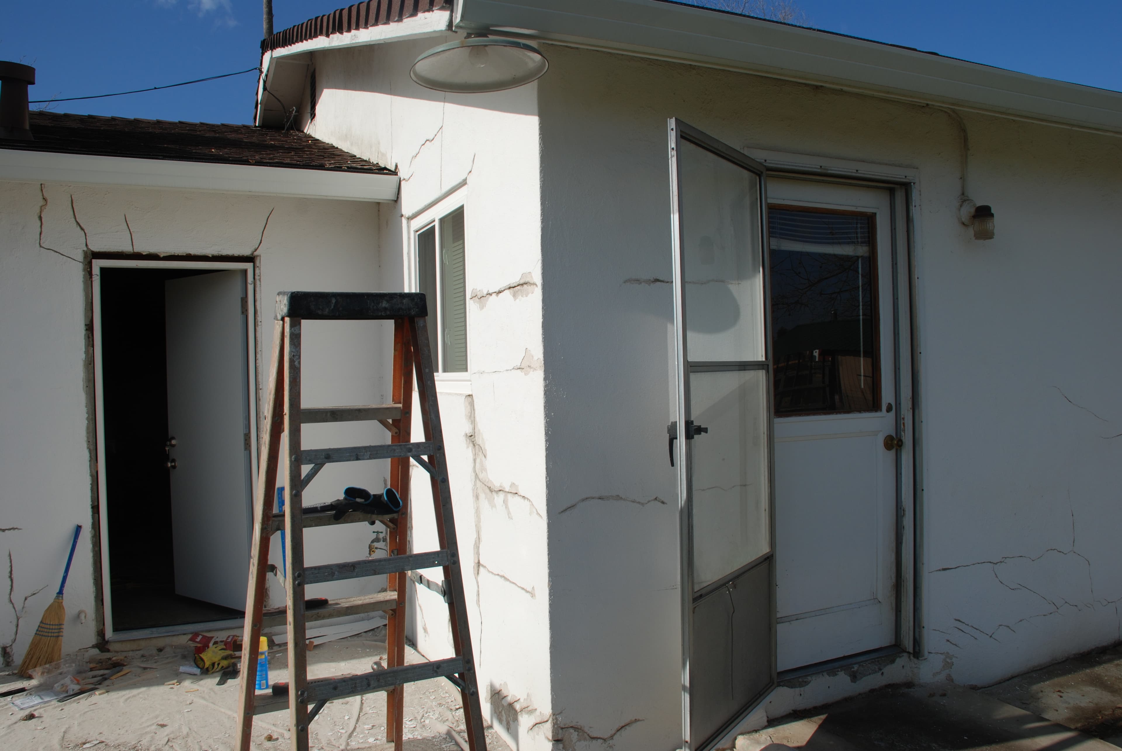 Wide stucco cracks running out from the corners of a door and a window on a white stucco home