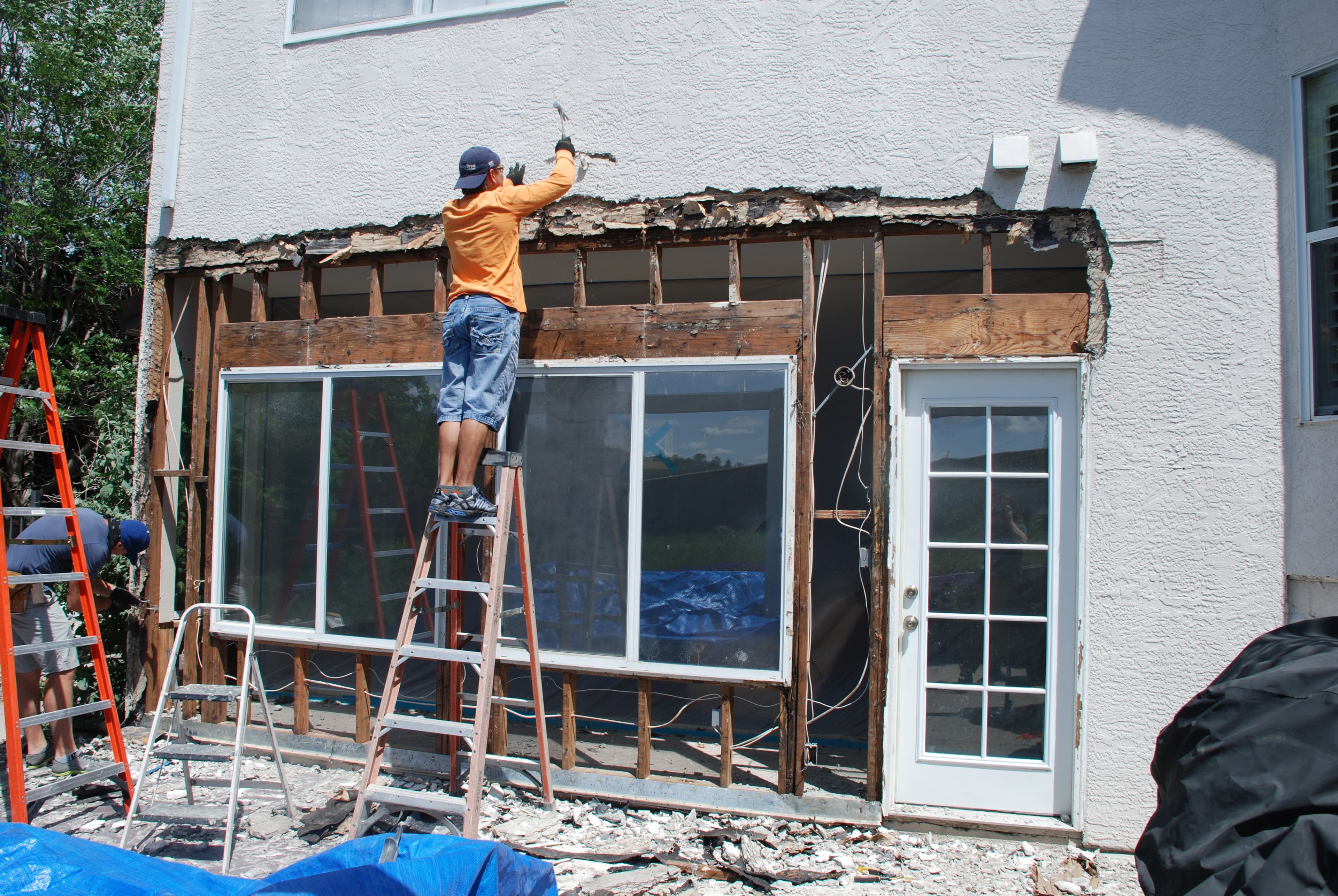 HomePRO crew removing damaged stucco and exposing framing around windows and a door during leak repair