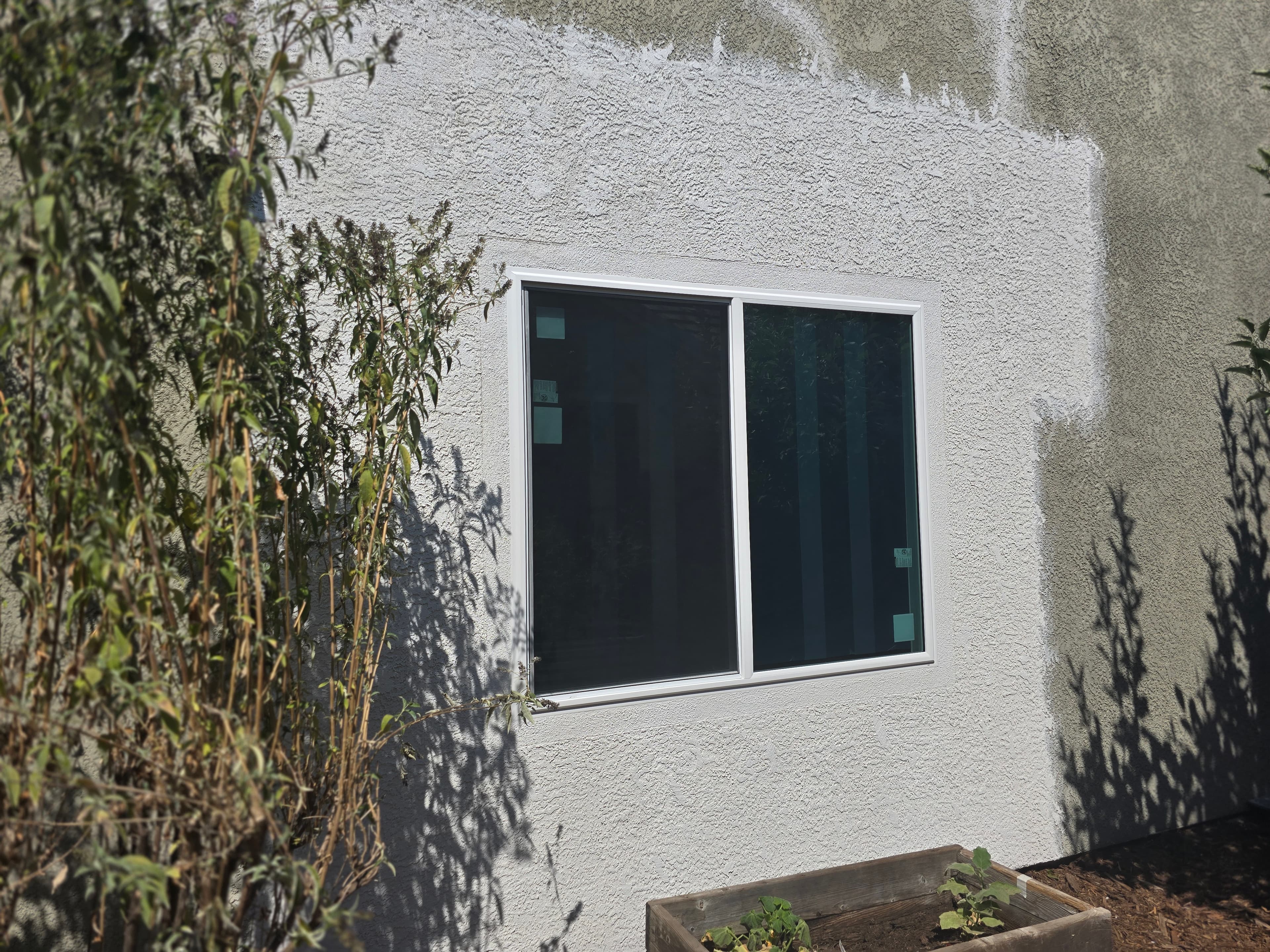 Newly applied light-colored stucco patching and texture surrounds a window on an exterior wall, contrasting with the older, darker stucco.